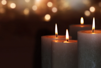 Closeup of of four lit pillar candles against a blurry background, illustrating that psychotherapy can help individuals experiencing grief cope with their loss.