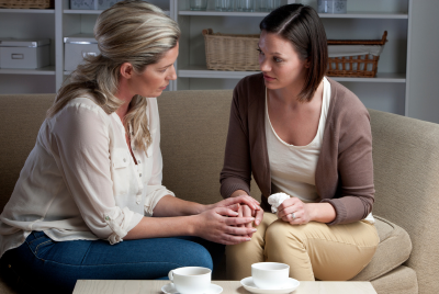 Image of two women sitting on a couch in a deep conversation, illustrating that there is no shame in seeking support to help process the complex emotions of grief.