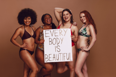 Four multi-ethnic women of varying sizes in bathing suits holding a sign that says, "Every body is beautiful"