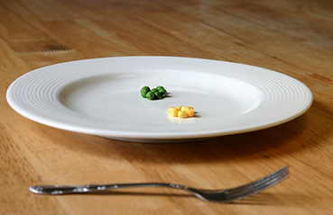 Image of a plate containing 4 peas and 4 kernels of corn, illustrating the concept that anorexia nervosa severely restricts calorie intake and can cause substantial harm to the body.