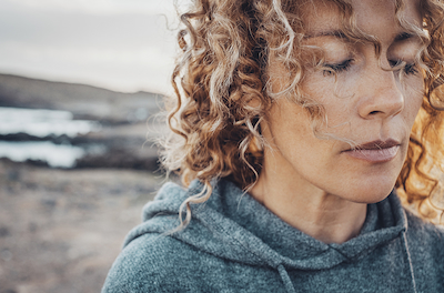 Close up image of a woman with her eyes closed, deep in thought against a beach background, illustrating that therapy can help you take back your life from anxiety.