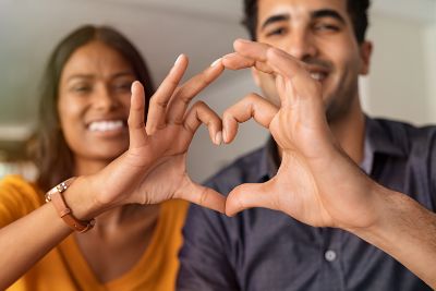 Close up of a smiling man and woman of color with hands forming a heart, illustrating that Healing Path Therapy helps you create healthy relationships.