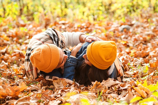 Head end view of a couple with yellow knit hats lying on the ground in autumn leaves, illustrating that seeking help from a professional trained in assisting couples and partners can help you heal your relationships