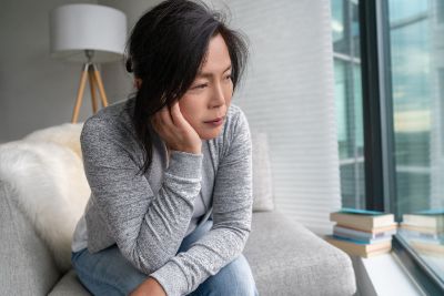 Asian young woman sitting on sofa with face resting on her hand illustrating that therapy can help manage symptoms of depression.