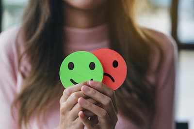 Close-up of a woman holding a smiley face and a frown face, illustrating that individuals with a personality disorder struggle to manage their thoughts, feelings, and actions in a flexible and healthy way.