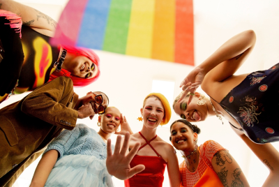Racially and gender diverse young people looking down at the camera with a rainbow flag illustrating that there are many gender identities, all of which are valid.