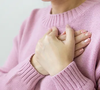closeup of hands over the heart of a woman wearing a pink sweater, illustrating an article about what happens when an empath leaves a narcissist